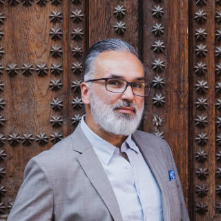 Photo of a latino man with grey hair wearing a suit