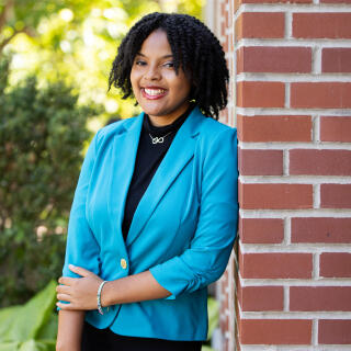 A smiling woman in a black dress and bright blue jacket