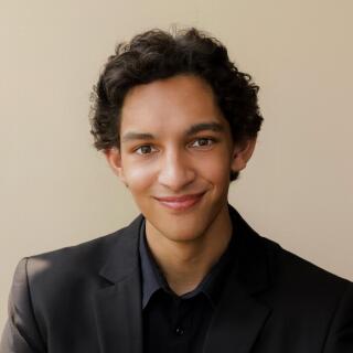 A smiling person in a black shirt and black jacket