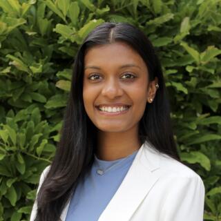 A smiling woman in a blue shirt and white jacket