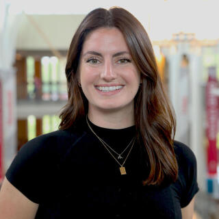 A smiling woman in a black t-shirt with gold necklaces